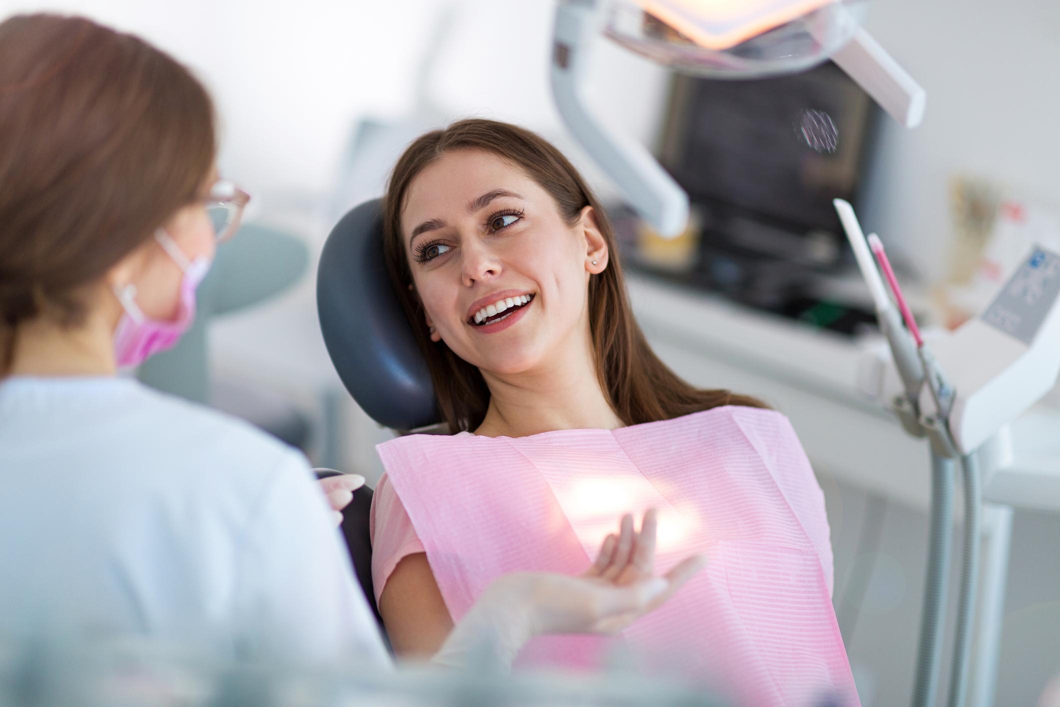 Woman patient smiling in a dental chair during a checkup, with dentist nearby wearing a mask