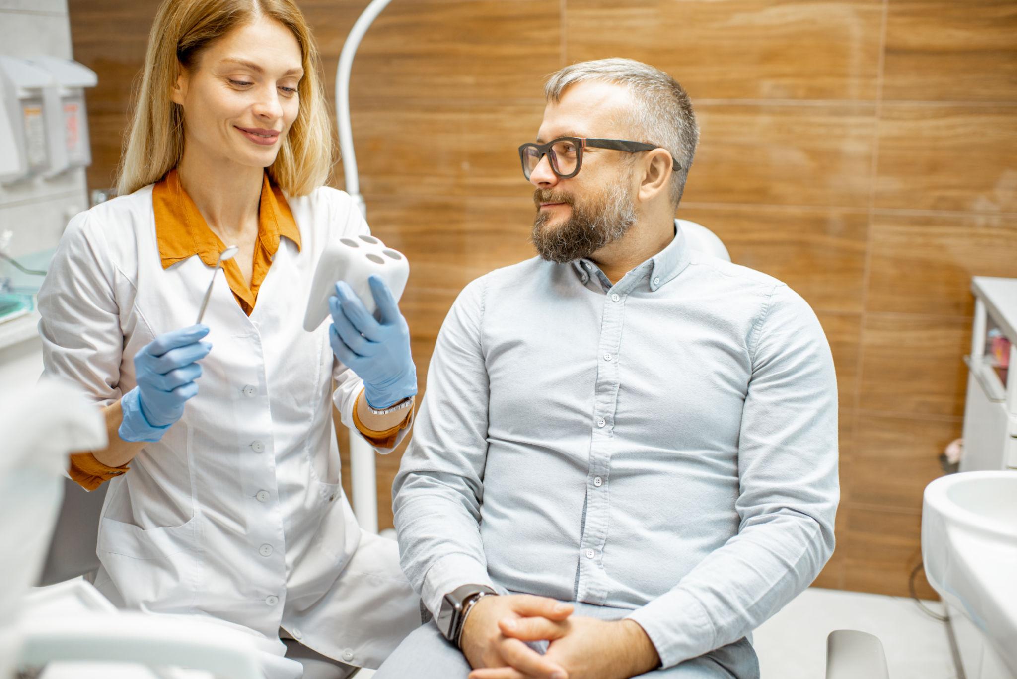 Dentist showing a dental impression tray to a male patient in a dental clinic.