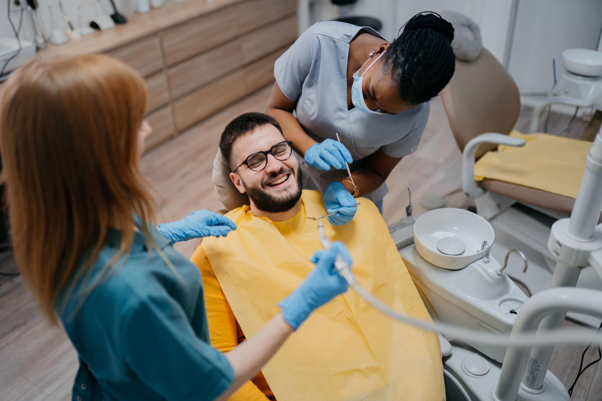 Dentist and assistant treating a patient in a dental chair, all wearing masks and gloves, with dental tools nearby.