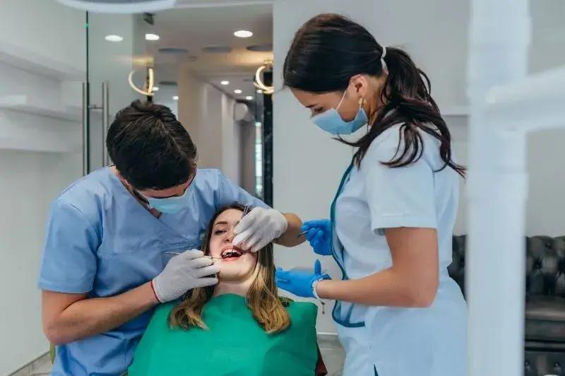 Dentist and dental assistant treating a patient in a bright dental clinic, all wearing masks and gloves.