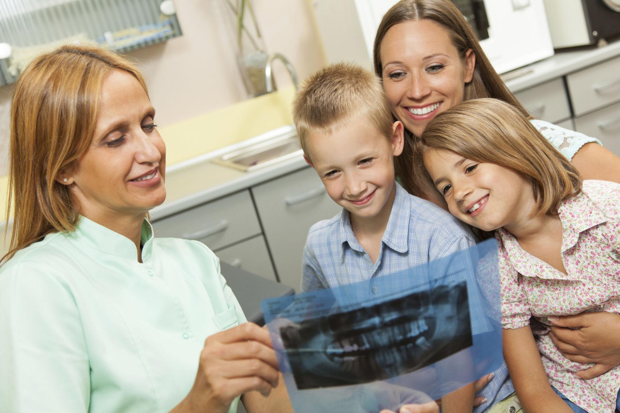 Dentist showing a dental X-ray to a smiling mother and her two children in a clinic setting