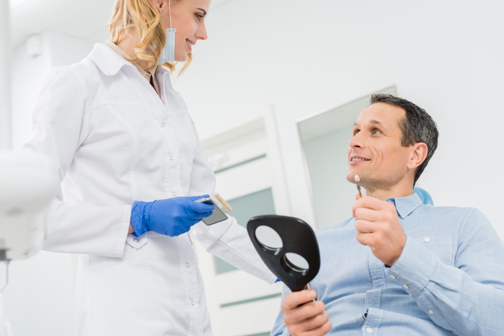 Dentist wearing a white coat and blue gloves talks with a patient in a dental clinic.