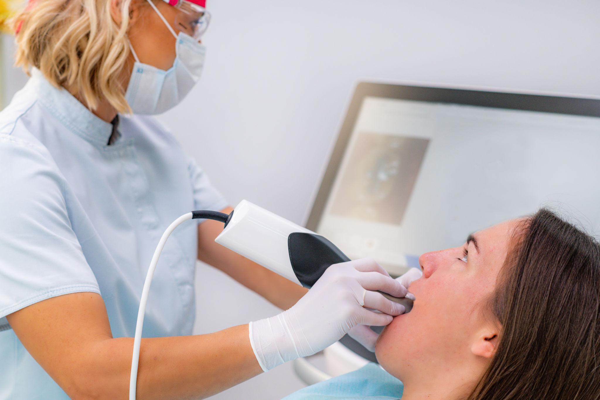 Dental professional in mask and gloves using a suction device on a patient relaxing in a dental chair.