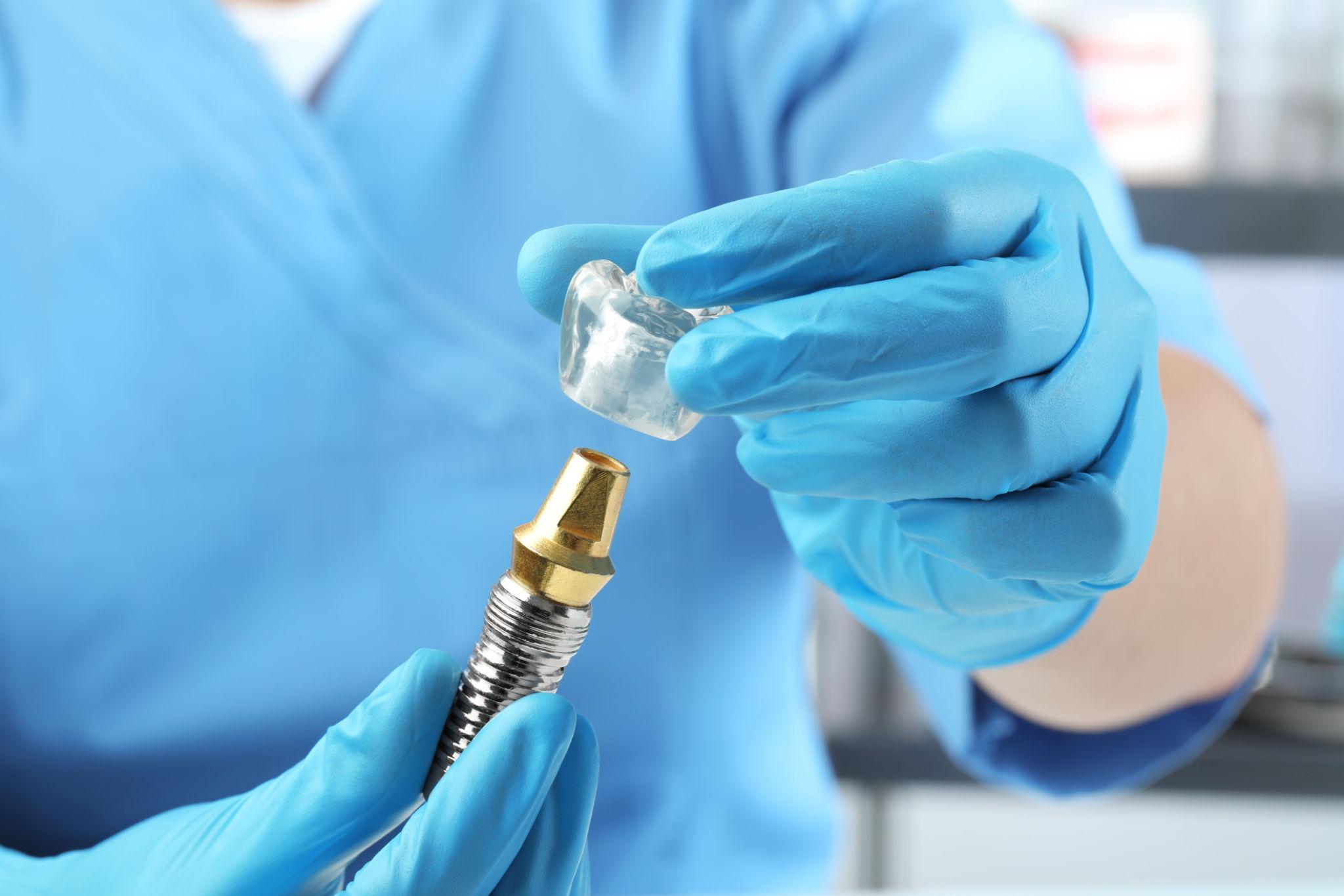 Close-up of gloved hands attaching a transparent tip to a dental drill.