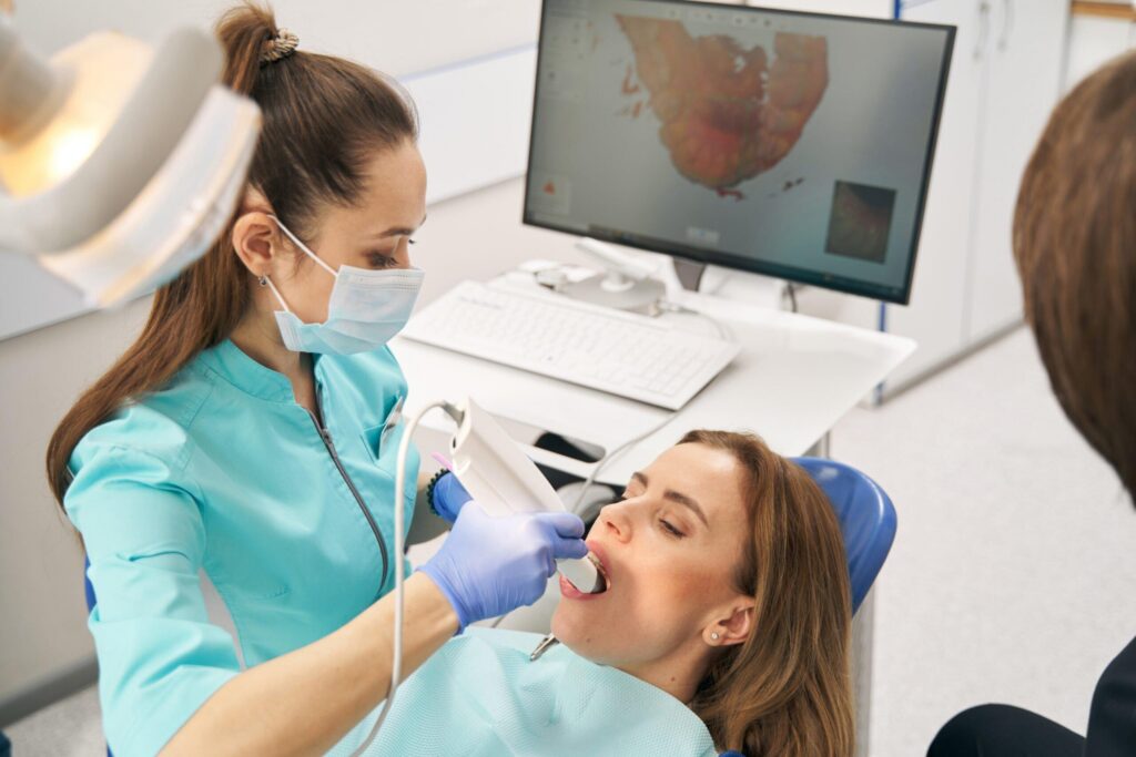 Dentist in teal scrubs and mask treating a patient in a dental chair with a monitor in the background.
