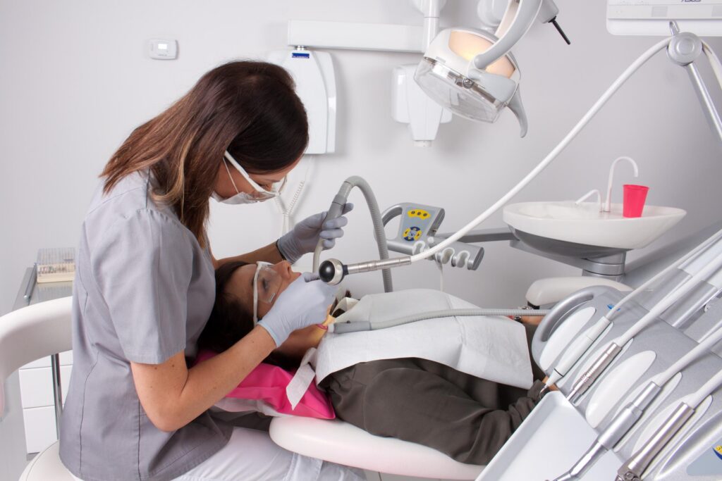 Dentist wearing a mask and gloves performing a dental procedure on a patient in a modern clinic with overhead light.